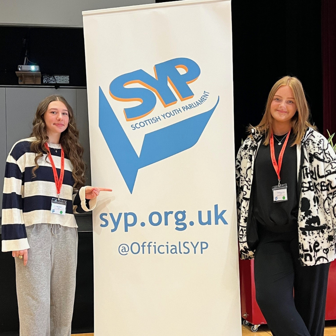 Rubie (left) and Chloe (right) standing next to a Scottish Youth Parliament pop-up banner at the recent sitting in Stirling.